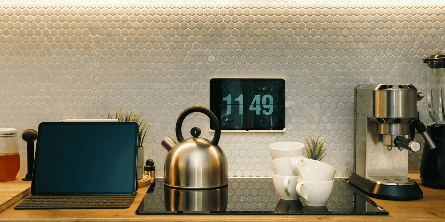 Kitchen counter with tablet, kettle, coffee machine, and digital clock.